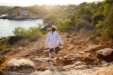 Naklejka premium Brunette girl in white cap hiking near the sea on sunset