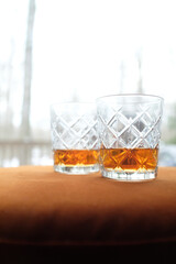 Two glasses of whiskey on orange velvet in cozy woods cabin