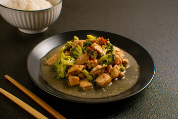 Delicious stir-fried chicken with broccoli served on a black plate with chopsticks and sauce, Asian homemade cuisine. Perfect for recipes, articles or any cooking content.