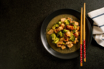 Delicious stir-fried chicken with broccoli served on a black plate with chopsticks and sauce, Asian homemade cuisine. Perfect for recipes, articles or any cooking content.