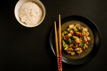 Delicious stir-fried chicken with broccoli served on a black plate with chopsticks and sauce, Asian homemade cuisine. Perfect for recipes, articles or any cooking content.