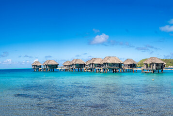 Traditional thatched roof abandoned cabins on stilts allow stretching out into the turquoise waters of the lagoon of Bora Bora, French Polynesia, South Pacific Ocean