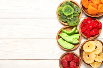 Bowls with different candied fruits on white wooden background