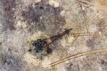 A rusty, collapsed power line tower stretches across a dry, desolate field, marked by vehicle tracks. It symbolizes infrastructure failure, decay, and environmental neglect