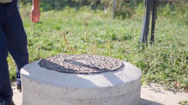 Individual in work attire opens a sewer manhole cover, revealing the interior, showcasing the process of accessing underground systems for maintenance and inspection purposes