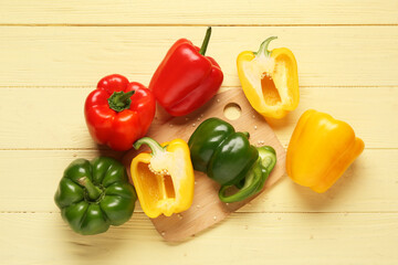 Cutting board with fresh colorful bell peppers on yellow wooden background