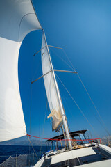 Fototapeta premium White sails filled with wind, seen from the bow of a sailing yacht near Croatia. Freedom, clean energy, adventure and mindful travel on the open sea.