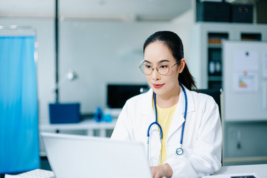 Asian female doctor using digital tablet to review medical data in hospital office. Concept of healthcare innovation, telemedicine, smart diagnosis, and real people professionalism.
