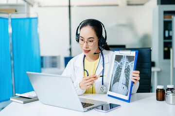 Asian female doctor wearing headset explaining X-ray via laptop. Concept of telemedicine, online...