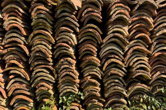 Curved roof tiles stacked in rows in sunlight
