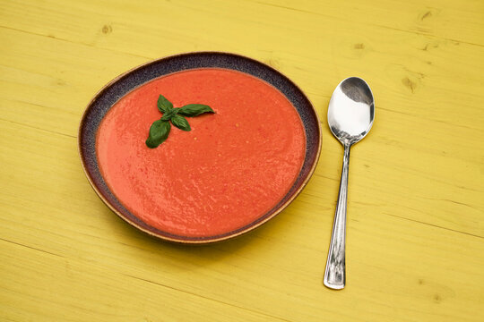 Still life of gazpacho garnished with basil in bowl next to spoon
