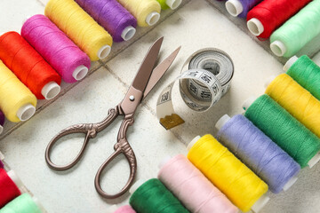 Colorful thread pools with scissors and measuring tape on white tile background