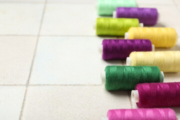 Colorful thread spools on white tile background