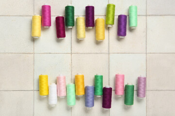 Colorful thread spools on white tile background