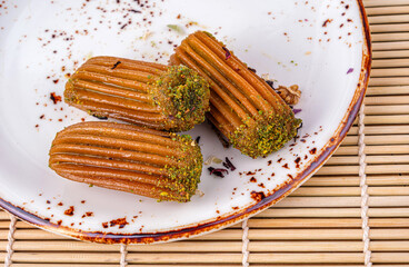 Close-up of three traditional Turkish tulumba desserts served on a rustic white ceramic plate, coated with syrup and garnished with crushed pistachios, placed on a bamboo mat in a cozy dining setting.
