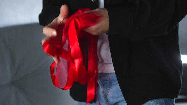 A man holds a long, tangled red satin ribbon and can't untangle it.
Close-up of an untangled skein of red satin ribbon.