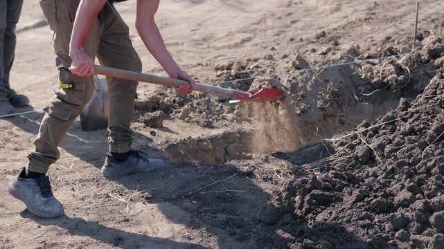 Worker using a shovel to dig a canal for communications installation, showcasing the action sequence with close-up details of the excavation process and surrounding earth