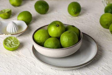 Bowl with fresh ripe limes and juicer on white background, closeup