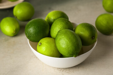 Bowl with fresh ripe limes on grunge background, closeup