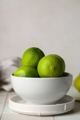 Bowl with fresh ripe limes on white tile table