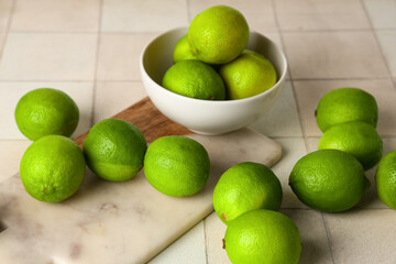 Bowl and cutting board with fresh ripe limes on white tile background