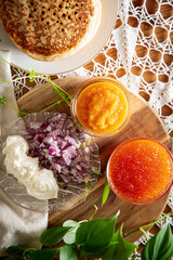 Rustic table setting with pancakes, caviar, sour cream, and onion - cozy homemade winter meal inspired by Nordic tradition.