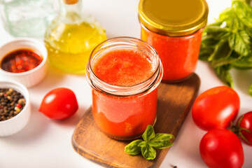 Homemade tomato sauce in glass jar with herbs and tomatoes nearby.