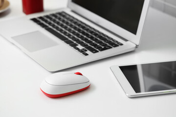 Modern computer mouse with laptop and tablet computer on table in office