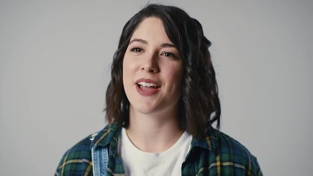 Smiling Young Woman Looking Directly at Camera with Warm and Friendly Expression Against a Clean Grey Background - Portrait of Happiness and Positivity for Busi