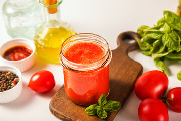 Homemade tomato sauce in glass jar with herbs and tomatoes nearby.