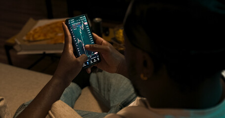 A trader observes financial indicators on his phone and laptop. Cryptocurrency chart movements and market analysis in progress. Shot from behind.