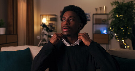 An attractive young man of multi-racial background wears a white shirt and black sweater. He adjusts his clothes nervously, preparing for a date and waiting for his girlfriend.
