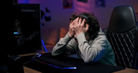 A young gamer experiences disappointment after a video game defeat. The child wears a headset,...
