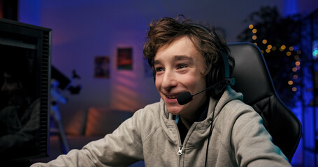 Emotion on the face of the boy playing computer games, focused child has a headset, excited mutiplayer shooter, online virtual world.