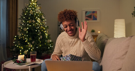 A handsome young boy, excited and happy, talks through a webcam on a laptop with his family while spending Christmas alone at home. He live unwraps a package, a gift he got from them.