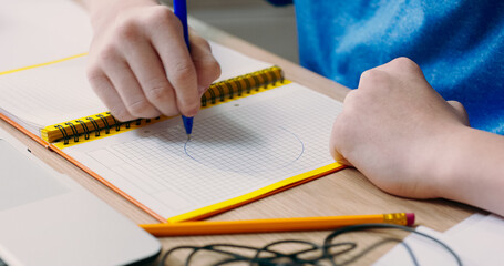 Child draws diagrams and shapes in a notebook, working on school tasks. His hands are focused on creating notes, learning through drawing and visual thinking.