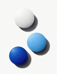 Three round pills, white, light blue, and dark blue, displayed in a studio setting against a white background.  Shadows subtly define the pills