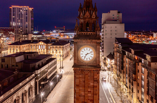 Drone photograph of the Albert Memorial Clock at night, framed by glowing city lights and a vibrant Belfast street below