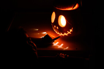 Child's hand touching glowing halloween jack-o'-lantern in dark