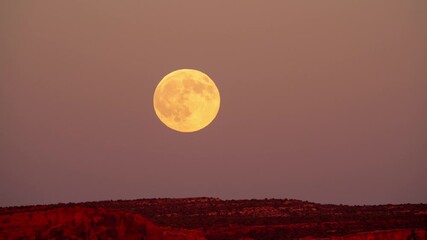 Timelapse of a large full moon rising over desert terrain as the sun is setting