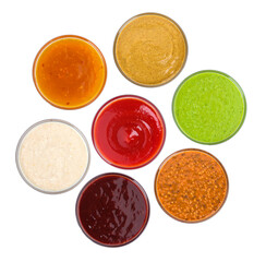 overhead photograph of seven small bowls of various colorful condiments and dipping sauces, including ketchup, mustard, and pesto, isolated on black.
