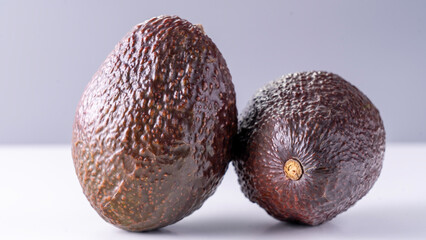 Two fully ripened, unpeeled avocados, captured in close-up against a white backdrop. High quality photo