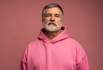 Caucasian smiling bearded mature man wearing pink hoodie against pink background
