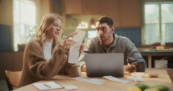 Couple Sitting at Home Behind a Laptop Computer, Managing Household Finances. Woman Reviews Bills and Receipts while the Man Enters Data, Both Focused and Drinking Coffee