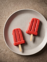 Two Red Fruit Popsicles on White Plate in Soft Studio Lighting