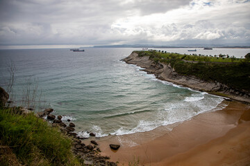 Scenic coastal view of a rocky beach with waves crashing and ships sailing under cloudy sky, perfect for travel and nature themes