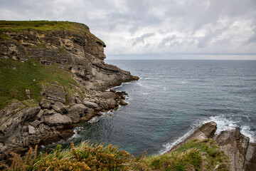 Scenic coastal cliffs overlooking the calm sea under a cloudy sky, showcasing rugged natural landscape and serene ocean views