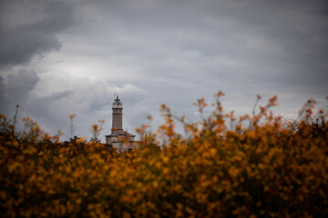 Overcast sky above the historic Faro de Cabo Mayor lighthouse partially obscured by vibrant orange wildflowers in a moody natural landscape setting