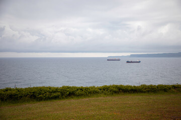 Peaceful coastal seascape with anchored cargo ships on calm waters under a cloudy sky, perfect for maritime and nature themes
