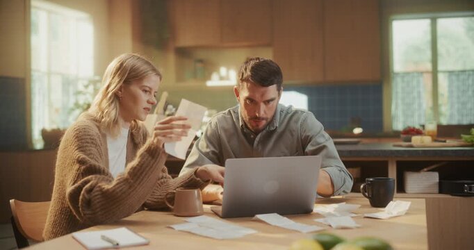 Young Caucasian Couple Managing Family Finances at Home. Female Goes Through Receipts and Payment Slips, while Male Calculates Costs and Inputs Data into Their Laptop Computer
